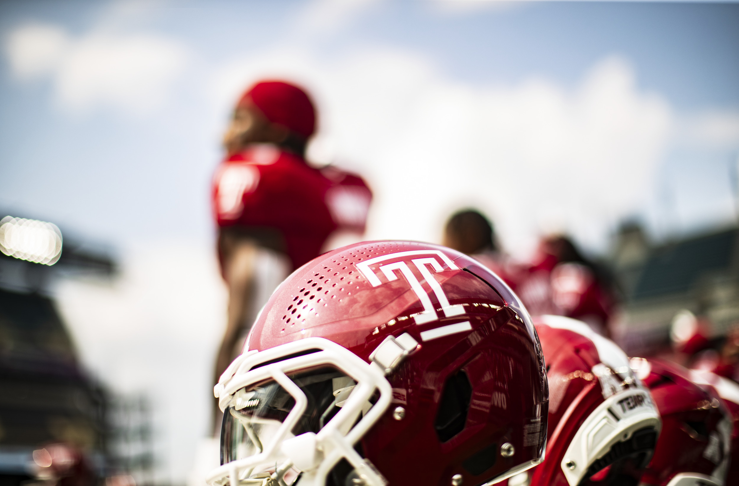 Image of cherry and white Temple football helmet with “T” logo on a stadium bench.